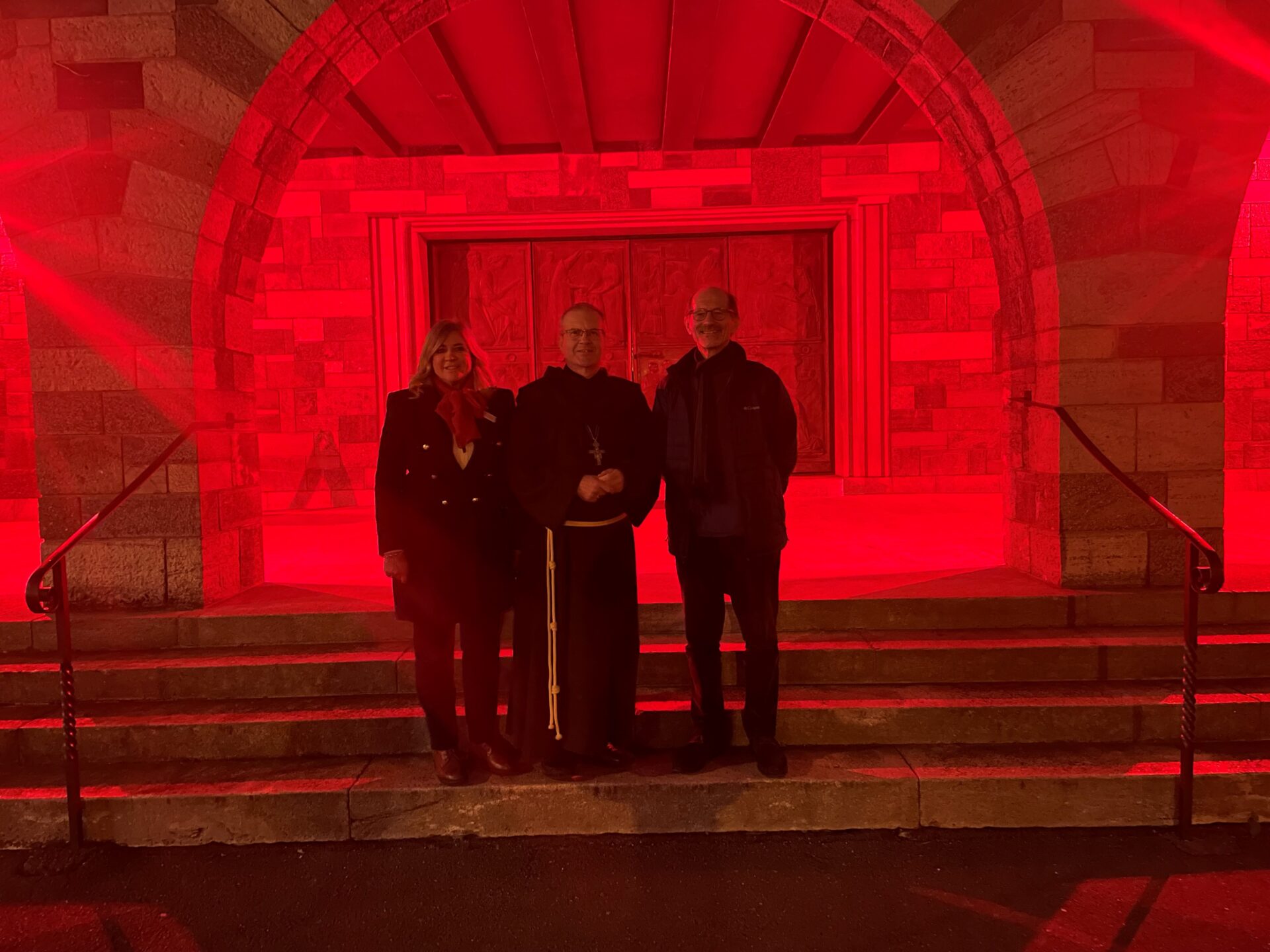 La chiesa di San Nicolao della Flüe a Lugano-Besso illuminata di rosso in occasione della RedWeek 2023. Nella foto, da sin. Lucia Wicki-Rensch (ACN), Mons Bugeja e don Marco Dania.
